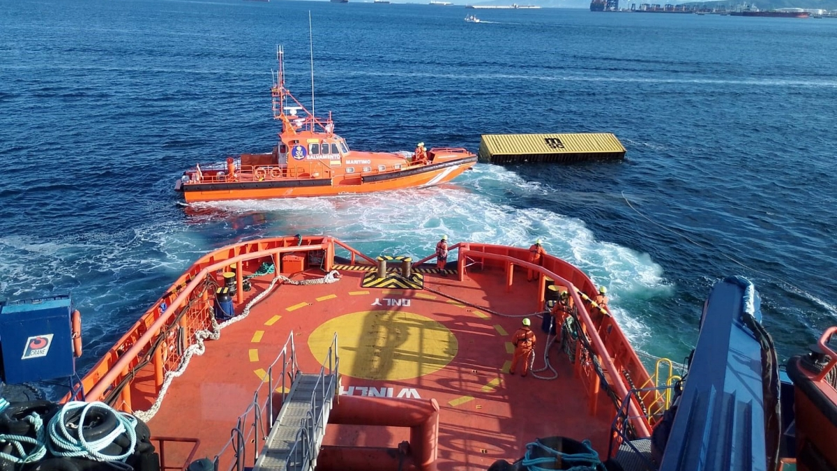 El contenedor de 20 pies flotando frente a la embarcación de Salvamento Marítimo y de fondo, el puerto de Algeciras
