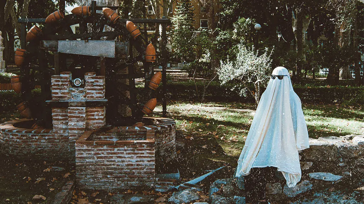 Fantasma moderno con gafas de sol posando junto a antigua noria de agua de ladrillo en un parque de Algeciras, ambiente oto&ntilde;al y misterioso.