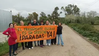 Grupo de familiares muestra una pancarta reivindicativa en una v&iacute;a rural de Jimena de la Frontera para exigir la recuperaci&oacute;n del transporte escolar.